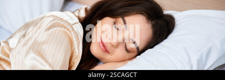 Una bella giovane donna gode di un sonno tranquillo indossando morbidi pigiami in raso nel suo comodo letto. Foto Stock