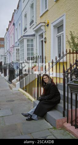 Donna seduta sui gradini di chelsea, londra, circondata da case colorate, trasuda un'atmosfera giovane ed elegante, catturando l'essenza di una vivace città Foto Stock