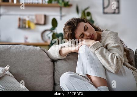 Una donna siede tranquillamente su un divano, perduta nel pensiero mentre affronta le sue emozioni. Foto Stock