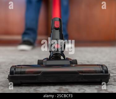 Primo piano ad angolo basso di un aspirapolvere cordless utilizzato su un pavimento con moquette. La composizione dinamica e lo sfondo sfocato conferiscono un'atmosfera piacevole Foto Stock