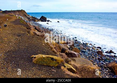 Costa rocciosa con spiaggia in lontananza. Le rocce sono sparse lungo il litorale Foto Stock