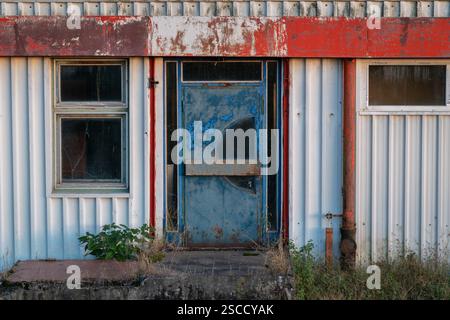Edificio industriale abbandonato con porte e finestre blu su entrambi i lati, vecchio edificio di panificio in lamiera ondulata Foto Stock