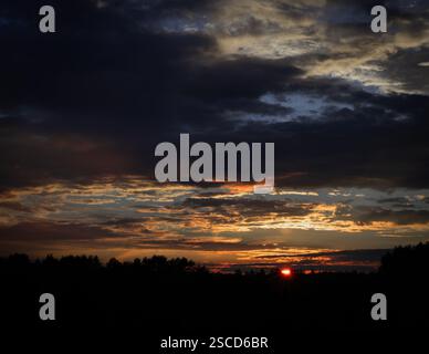Un tramonto suggestivo con nuvole profonde e testurizzate che proiettano ombre spettacolari sul cielo. La luce dorata che attraversa l'oscurità crea un powerfu Foto Stock