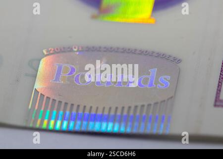 Primo piano di un elemento di sicurezza su una banconota, che mostra un'iscrizione olografica "libbre" con effetto iridescente arcobaleno e micro-testo ripetuto. Foto Stock