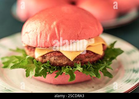 Delizioso Burger rosa con formaggio e pesce o cotoletta di manzo con lattuga su un piatto chiaro su sfondo verde scuro. Primo piano. Foto di alta qualità Foto Stock