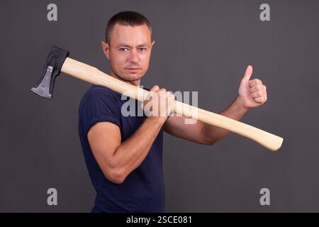 un uomo con un'ascia che mostra il pollice su sfondo grigio. Foto Stock