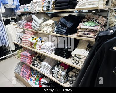 Kiev, Ucraina - 5 febbraio 2025: T-shirt impilate in vari colori e disegni organizzati negli scaffali di un negozio di abbigliamento Foto Stock