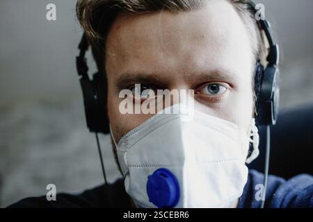 Primo piano di un uomo con maschera e cuffie, che sembra concentrato in interni Foto Stock