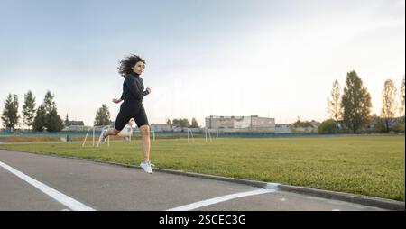 Una donna che corre su una pista accanto a un campo aperto durante il tramonto Foto Stock