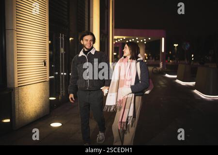 Una scena notturna della città con una coppia che cammina mano nella mano, sorridendo Foto Stock
