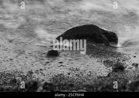 Una fotografia in bianco e nero a lunga esposizione che cattura il movimento dell'acqua intorno a una roccia testurizzata. Foto Stock