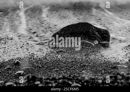 Una fotografia in bianco e nero a lunga esposizione che cattura il movimento dell'acqua intorno a una roccia testurizzata. Foto Stock