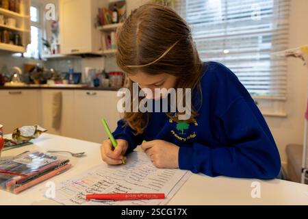 Una studentessa di nove anni pratica i compiti di ortografia sul tavolo della cucina a casa. Foto Stock