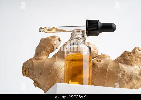 Olio di zenzero giallo in flacone contagocce che presenta il prodotto sul podio bianco Foto Stock