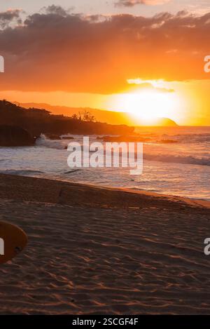 Tramonto su Hawaiian Beach con tavola da surf e scogliere rocciose Foto Stock