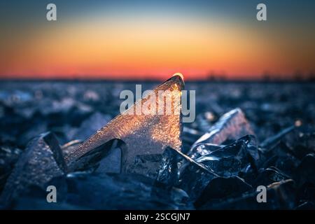 Fonyod, Ungheria - cubetti di ghiaccio trasparenti sul lago Balaton ghiacciato in un freddo pomeriggio invernale con sole tramonti dorati e un colorato tramonto cielo sole behi Foto Stock