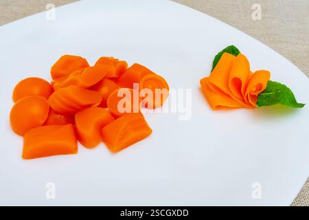 Su un piatto bianco è esposta una vasta gamma di dolci arancioni. Gli articoli variano di forma, con una rosa arancione decorativa realizzata con la stessa swe Foto Stock