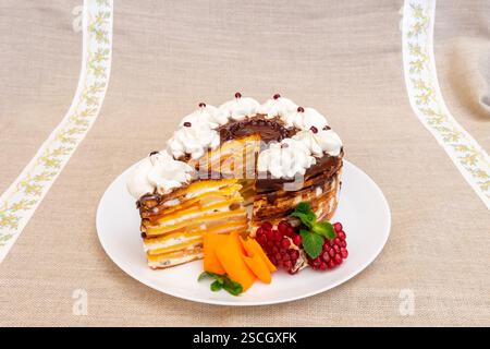 Una torta a strati splendidamente presentata si stende su un piatto bianco. La torta presenta più strati di panna e cioccolato, ricoperti di c Foto Stock