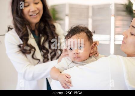 Medico che valuta il bambino mentre la mamma lo tiene in braccio Foto Stock