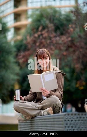 Una donna ama leggere un libro all'aperto mentre è seduta su una panchina Foto Stock