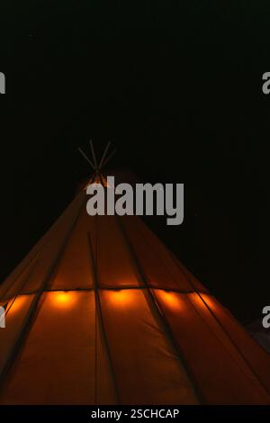 Una tenda si illumina di calore sotto un cielo scuro e pieno di stelle nella Lapponia svedese, creando un'atmosfera serena e accogliente. Ideale per viaggi, avventure e n Foto Stock