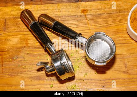 Due portafiltri della macchina per caffè espresso poggiano su un bancone in legno, mostrando i cestelli e i manici in metallo. Foto Stock