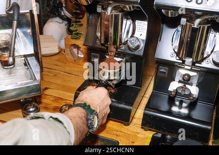 Un barista macina i chicchi di caffè freschi in un portafiltro utilizzando un macinacaffè professionale. Il bancone della caffetteria presenta attrezzature di alta qualità Foto Stock