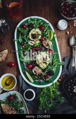 Un'insalata vivace con avocado, fichi, ciliegie e verdure miste su un rustico tavolo in legno. Gli ingredienti freschi creano un piatto colorato e appetitoso Foto Stock
