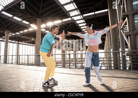Una vivace coppia gay gode di un momento di gioco in un ambiente urbano. Una persona, indossando un abbigliamento colorato, balla energicamente mentre l'altra cattura Foto Stock