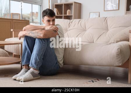 Giovane preoccupato seduto a terra a casa Foto Stock
