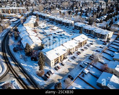 Paesaggio urbano innevato con un grande complesso di appartamenti e un parcheggio. La neve ricopre il terreno e gli edifici, dando alla scena un ambiente tranquillo e Foto Stock