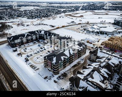 Paesaggio urbano innevato con un grande complesso di appartamenti in primo piano. Il complesso di appartamenti è circondato da parcheggi e dispone di un gran numero di auto Foto Stock