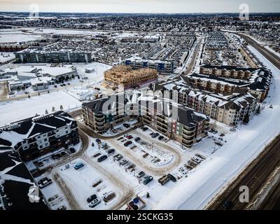 Paesaggio urbano innevato con un grande complesso di appartamenti nel centro. Il complesso di appartamenti è circondato da un parcheggio con diverse auto parcheggiate al suo interno. Con Foto Stock