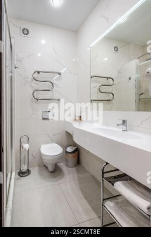 Bagno luminoso ed elegante con box doccia in vetro, WC a parete e piastrelle effetto marmo per un aspetto elegante e lussuoso. Foto Stock