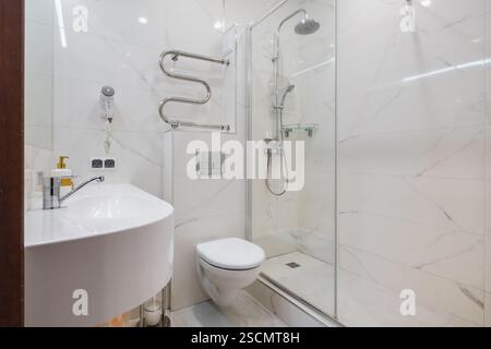 Bagno luminoso ed elegante con box doccia in vetro, WC a parete e piastrelle effetto marmo per un aspetto elegante e lussuoso. Foto Stock