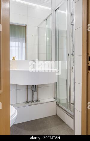 Bagno luminoso ed elegante con box doccia in vetro, WC a parete e piastrelle effetto marmo per un aspetto elegante e lussuoso. Foto Stock