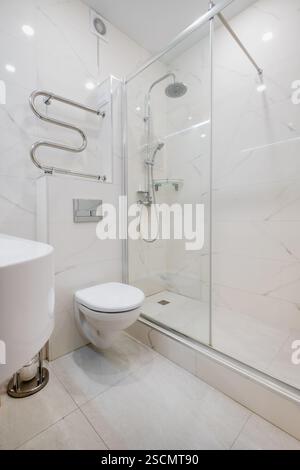 Bagno luminoso ed elegante con box doccia in vetro, WC a parete e piastrelle effetto marmo per un aspetto elegante e lussuoso. Foto Stock