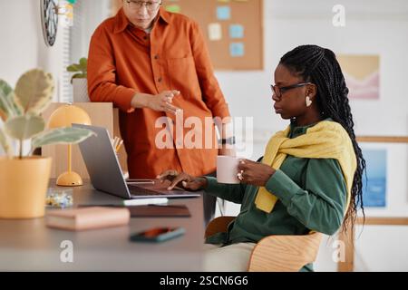 Collaborare in un ambiente d'ufficio moderno con persone diverse che condividono idee. Utilizzando tecnologie moderne e abbigliamento casual, i partecipanti lavorano su attività creative e si impegnano in discussioni Foto Stock
