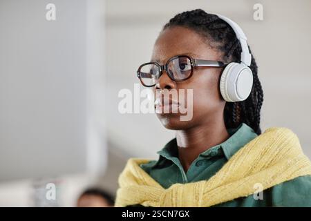 Indossando occhiali e cuffie individuali, l'aspetto è concentrato e assorbito dal pensiero. Indossa un maglione giallo su una camicia verde Foto Stock