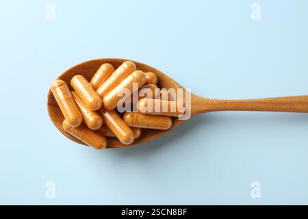 Capsule di curcuma in cucchiaio di legno su sfondo azzurro, vista dall'alto Foto Stock