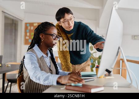 Due colleghi che analizzano i dati su uno schermo di un computer in un ufficio, impegnati in un lavoro collaborativo. Uno indossa gli occhiali osservando attentamente mentre spiega i dettagli Foto Stock
