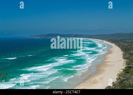 Una vista serena che mostra l'ampia costa della spiaggia di sego vicino a Byron Bay, NSW, Australia. Cieli azzurri, onde turchesi vibranti e lussureggianti Foto Stock