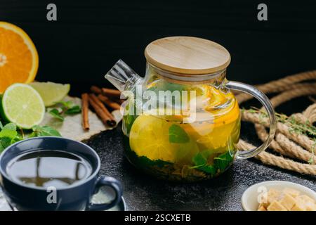 Tè agli agrumi alle erbe con menta fresca, lime, arancia e zucchero di canna servito in una teiera di vetro e tazza Foto Stock