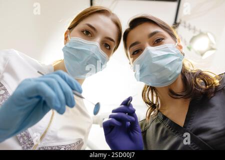 Dal basso dentisti con specchio e dispositivo piegato sopra la paziente durante l'appuntamento in clinica odontoiatrica. Foto Stock