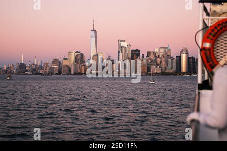 Una vista d'ora d'oro dello skyline di Manhattan dal fiume Hudson. Il One World Trade Center brilla mentre le barche scivolano sull'acqua. Foto Stock