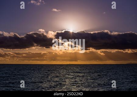 Un tramonto mozzafiato si dispiega sull'oceano, con colori vivaci che si riflettono nell'acqua mentre le nuvole spargono la luce dal sole che tramonta. La tranquillità della Foto Stock