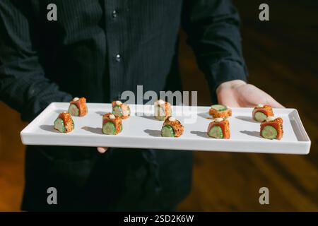 Il piatto offre colorati sushi roll serviti da un membro del personale di catering in un ambiente elegante durante un'occasione speciale. Foto Stock