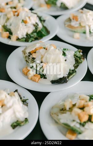 Insalate colorate con verdure, condimento cremoso e crostini sono disposte su piatti bianchi per il piacere degli ospiti. Foto Stock