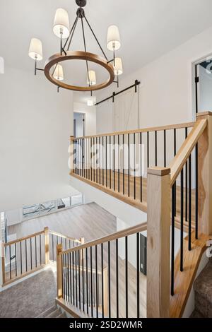 Scala a chiocciola con lampadario appeso al soffitto. Il lampadario è realizzato in legno e ha una base bianca. La scala si trova in una grande Foto Stock
