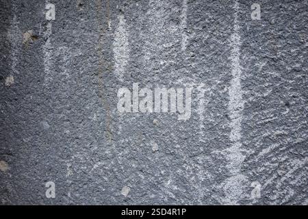Una parete grigia testurizzata mostra imperfezioni naturali e una finitura ruvida. Varie sfumature e motivi creano un effetto visivo interessante, evidenziando Foto Stock